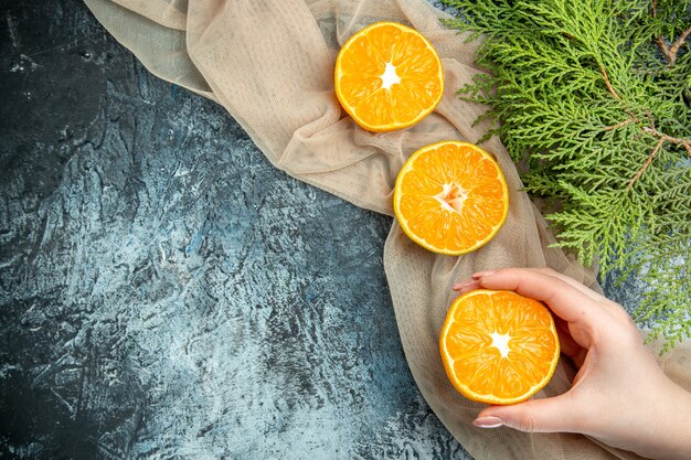 Draufsicht geschnittene Orangen in den weiblichen Hand-Tannenzapfen auf beigem Schal auf freiem Raum der dunklen Oberfläche