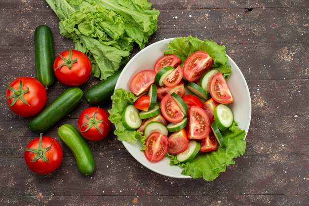 Draufsicht geschnittene Tomaten mit Gurken in weißer Platte mit grünem Salat auf braunem, frischem Gemüsesalat mit Lebensmittelgemüse