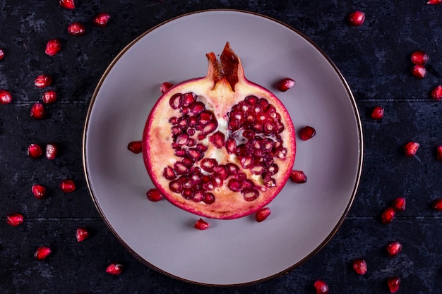 Kostenloses Foto draufsicht geschnittenen granatapfel auf einem weißen teller auf einem schwarzen tisch