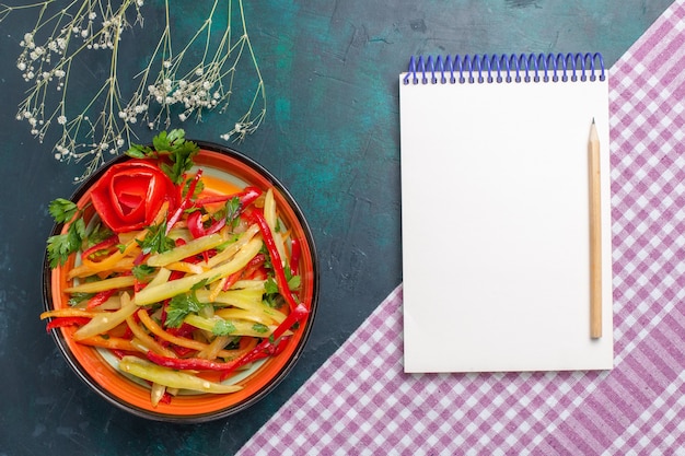 Draufsicht geschnittener Paprika farbiger würziger Salat mit Notizblock auf dunkelblauem Schreibtisch