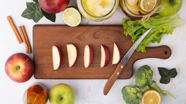 Draufsicht geschnittener roter Apfel auf einem Brett mit Zitronentee frischem Apfelsaft Brocoli Zimtscheibe Limette und Salatblatt