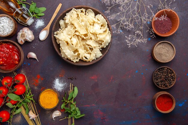 Draufsicht geschnittener Teig mit Gewürzen und Tomaten auf dunklem Schreibtischmahlzeit-Teignahrungsmittel-Nudelabendessen