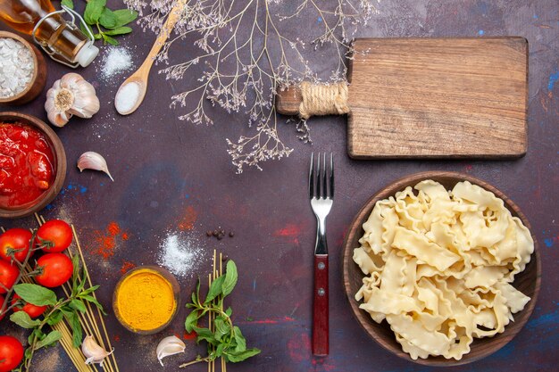 Draufsicht geschnittener Teig mit Tomatensauce und Tomaten auf dunklem Hintergrund Teignudel-Nudel-Abendessen