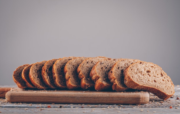 Draufsicht geschnittenes Brot im Schneidebrett auf Holztisch und grauer Oberfläche