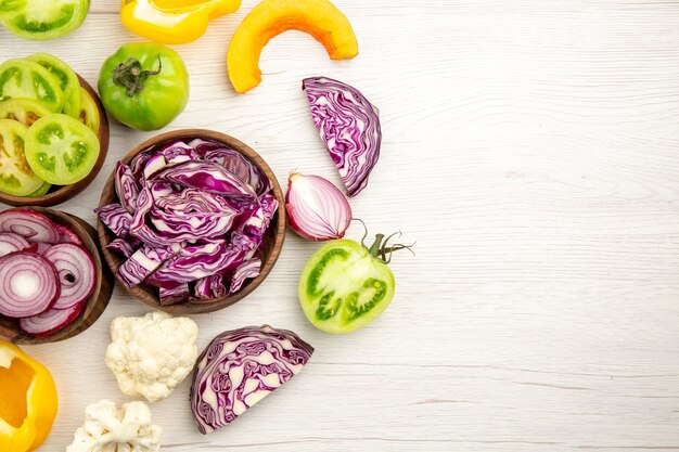 Draufsicht geschnittenes Gemüse Rotkohlgrüner Tomatenkürbis rote Zwiebel Paprika Blumenkohl Zitrone in Holzschalen auf weißer Holzoberfläche Freiraum