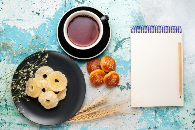 Draufsicht getrocknete Ananasringe mit Tasse Tee und kleinen Kuchen auf dem blauen Hintergrund Fruchtananas trockener süßer Zucker