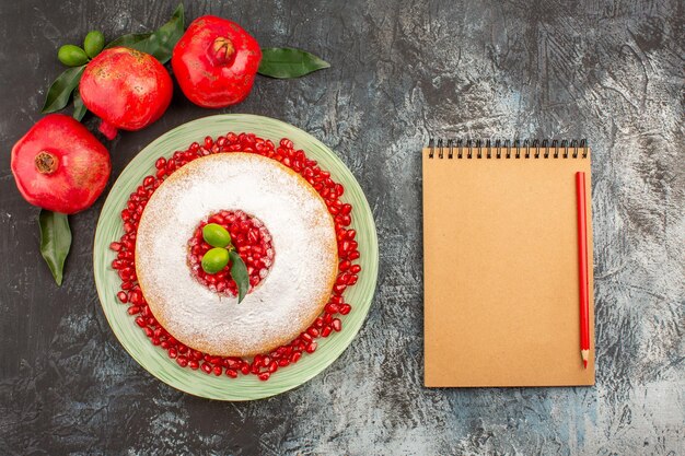 Draufsicht Granatäpfel ein appetitlicher Kuchen drei Granatäpfel mit Blättern Notizbuch und Bleistift