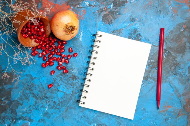 Draufsicht Granatapfelkerne in Holzschale mit verstreuten Samen gelegt ein Notizbuch ein Bleistift auf blauem Hintergrund