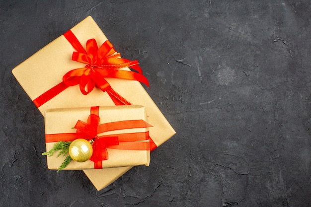 Draufsicht große und kleine Weihnachtsgeschenke in braunem Papier mit rotem Band auf dunkler Oberfläche gebunden