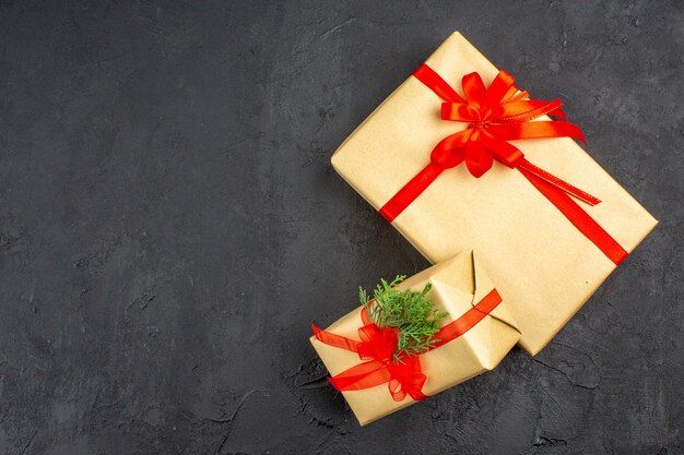 Draufsicht große und kleine Weihnachtsgeschenke in braunem Papier mit rotem Bandzweig Tanne auf dunkler Oberfläche gebunden