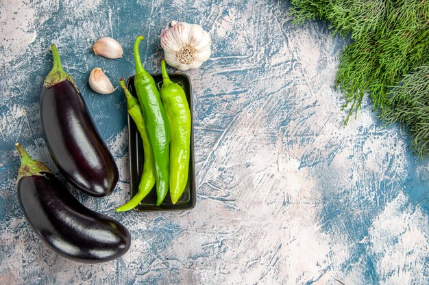 Draufsicht grüne Peperoni auf schwarzem Teller Knoblauch Auberginen auf blau-weißem Hintergrund