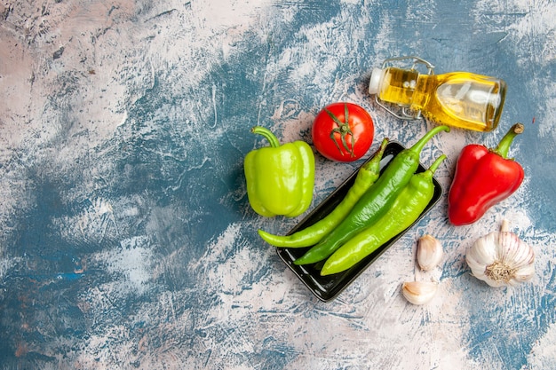 Draufsicht grüne Peperoni auf schwarzem Teller Tomaten rote und grüne Paprika Knoblauchölflasche auf blau-weißem Hintergrund