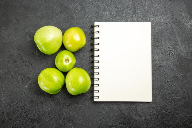 Draufsicht grüne Tomaten ein Notizbuch auf dunkler Oberfläche