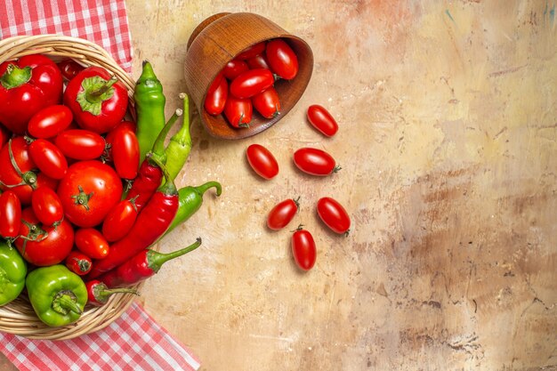 Draufsicht grüne und rote Paprikaschoten Tomaten in Weidenkorb verstreute Kirschtomaten aus Schüssel Küchentuch auf bernsteinfarbenem Hintergrund