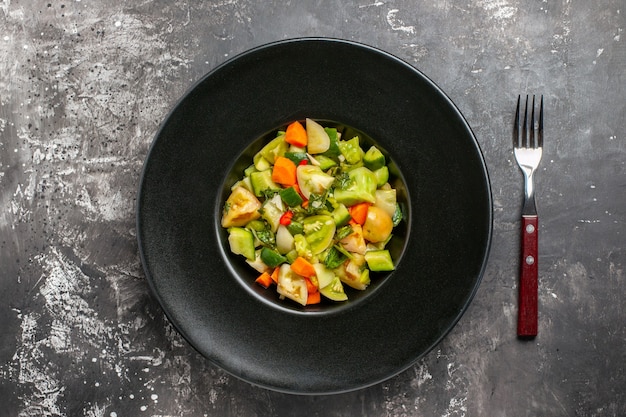 Draufsicht grüner Tomatensalat auf ovalem Teller eine Gabel auf dunklem Hintergrund