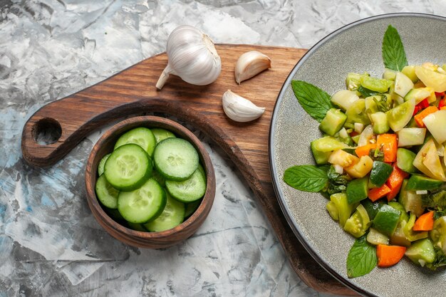 Draufsicht grüner Tomatensalat auf ovalem Teller Knoblauch auf Schneidebrett Schüssel mit geschnittenen Gurken auf dunklem Hintergrund