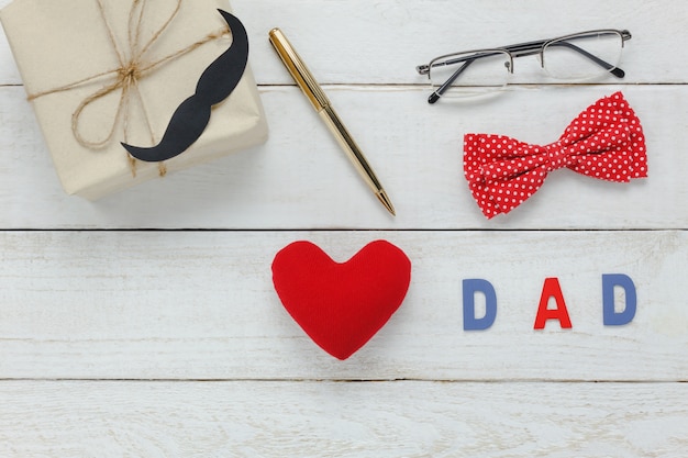 Draufsicht Happy Father Tag .Red Herz und Wort &quot;DAD&quot; auf rustikalen hölzernen Hintergrund. Zubehör mit Schnurrbart, Vintage Fliege, Stift, Gegenwart und Brille.