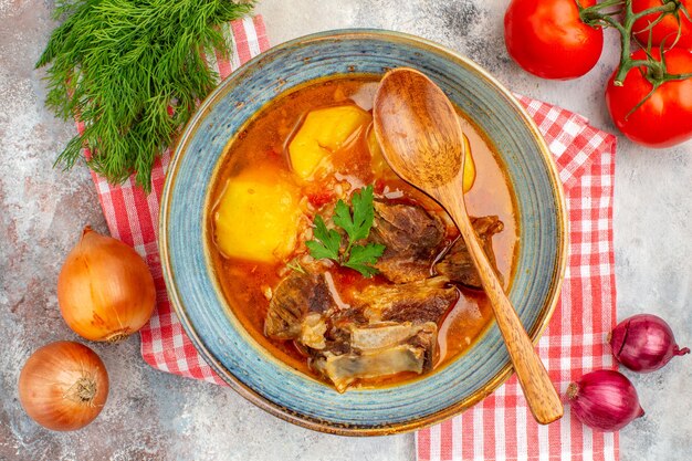 Draufsicht hausgemachte Bozbash-Suppe Holzlöffel Küchentuch ein Bündel Dilltomaten Zwiebeln auf nacktem Hintergrund