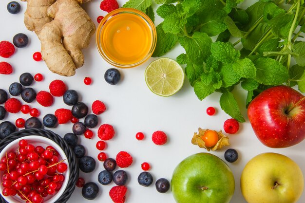 Draufsicht Himbeeren mit Honig, Äpfeln, Blaubeeren, roten Johannisbeeren, Zitrone, Ingwer, Minzblättern auf weißer Oberfläche horizontal