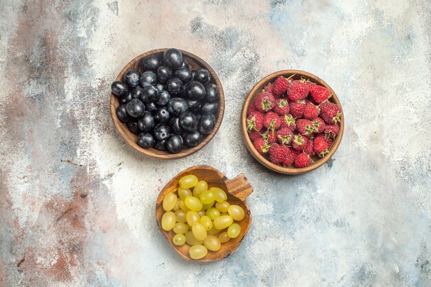 Draufsicht Himbeeren schwarze und gelbe Trauben in Schalen auf grauem isoliertem Oberflächenfreiraum