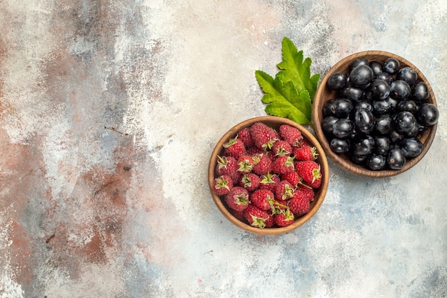 Draufsicht Himbeeren und Trauben in Schalenblättern auf grauer isolierter Oberfläche mit Kopierraum