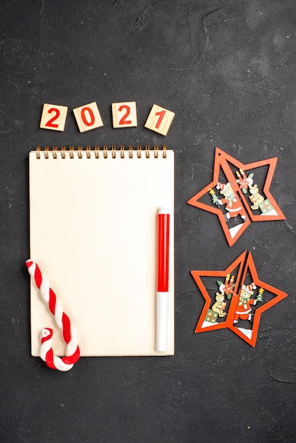 Draufsicht Holzblock roter Marker Weihnachtsbonbons auf Notebook-Weihnachtsbaumschmuck auf dunklem, isoliertem Hintergrund