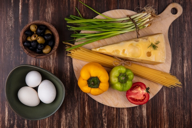 Draufsicht hühnereier in schüssel mit oliven frühlingszwiebeln paprika und scheibe maasdam käse mit tomate auf holzhintergrund