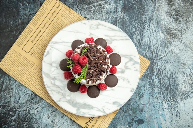 Draufsicht-Käsekuchen mit Schokolade und Himbeeren auf weißer ovaler Plattenzeitung auf grauer Oberfläche freiem Raum