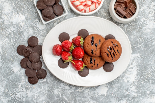 Draufsicht Kekse Erdbeeren und runde Pralinen auf den ovalen Tellerschalen mit Bonbonpralinen und runden bitteren Pralinen auf dem grauweißen Tisch