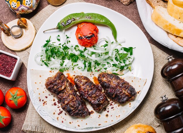 Draufsicht Khan Kebab auf Fladenbrot mit Tomaten und gegrilltem Pfeffer mit Zwiebeln und Kräutern