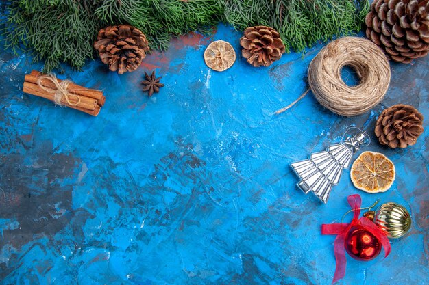 Draufsicht kiefer zweige strohfaden zimtstangen getrocknete zitronenscheiben weihnachtsbaum spielzeug auf blau-roter oberfläche