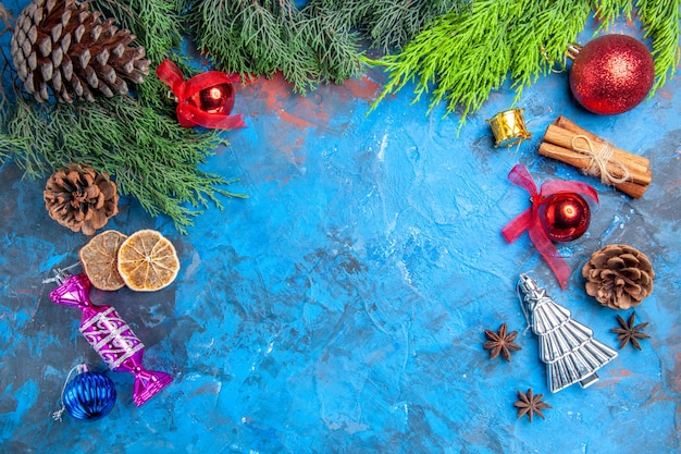 Draufsicht kiefer zweige tannenzapfen weihnachtsbaum spielzeug anis samen getrocknete zitronenscheiben auf blau-rotem hintergrund