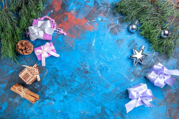 Draufsicht Kiefer Zweige Weihnachtsbaum Spielzeug Weihnachtsgeschenke Zimtstangen auf blau-roter Oberfläche