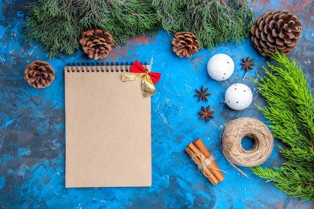 Draufsicht kiefernzweige strohfaden zimtstangen anissamen weiße weihnachtsbaumkugeln ein notizbuch auf blau-roter oberfläche