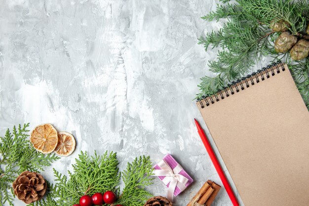 Draufsicht Kieferzweige kleines Geschenk Weihnachtsbaum Spielzeug Notizbuch Bleistift getrocknete Zitronenscheiben auf grauem Hintergrund