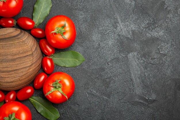 Draufsicht Kirschbaum und rote Tomaten Lorbeerblätter um einen Holzteller auf der linken Seite des dunklen Bodens mit Kopierspase