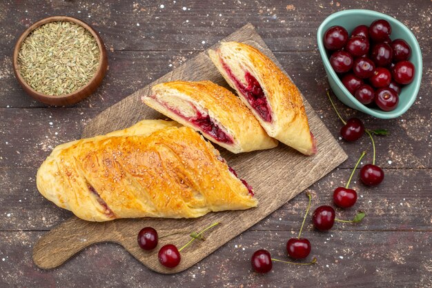 Draufsicht Kirschgebäck köstlich und süß mit frischen Sauerkirschen auf dem braunen hölzernen Schreibtischgebäckkuchen-Kekszuckersüß