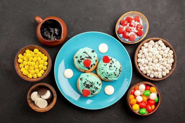 Draufsicht kleine cremige Kuchen mit Bonbons auf der dunkelgrauen Oberfläche Dessertkuchen Keksfarbe Süßigkeitenkeks