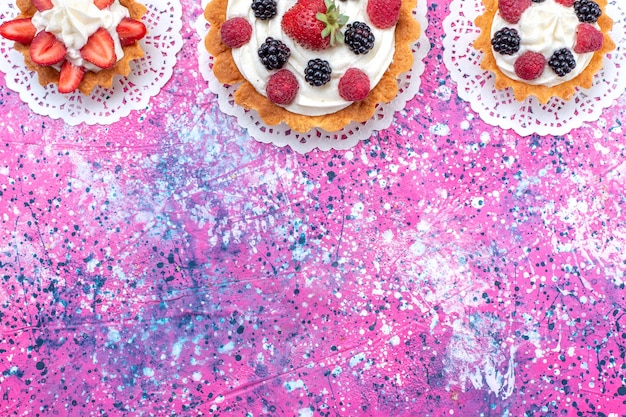 Draufsicht kleine cremige Kuchen mit verschiedenen Beeren auf dem hellen Hintergrundkuchen-Keksbeeren-süßen Auflauf