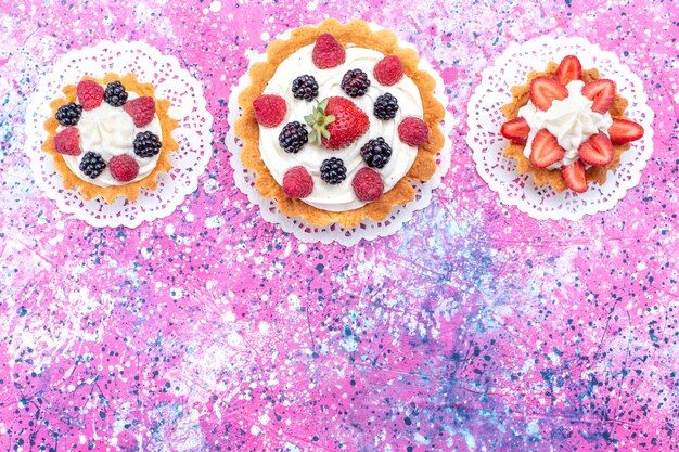 Draufsicht kleine cremige Kuchen s mit Beeren auf dem hellen weißen Hintergrundkuchen-Keks-Beeren-süßen Backfoto