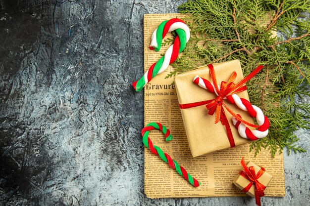 Draufsicht kleine Geschenke mit rotem Band Weihnachtsbonbons auf Zeitungskiefernzweigen auf grauer Oberfläche gebunden