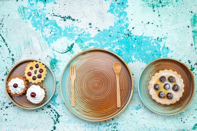 Draufsicht kleine köstliche Kuchen mit Sahne und Früchten auf hellblauem Hintergrundkuchen süße Sahne backen Frucht