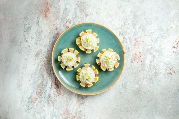 Draufsicht kleine köstliche Kuchen mit Sahne- und Zitronenscheiben auf weißem Oberflächenkuchenkeksplätzchen süßer Teezucker
