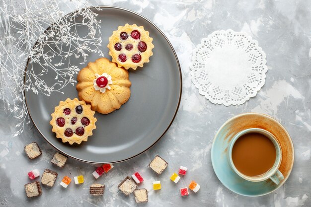 Draufsicht kleine Kuchen innerhalb der grauen Platte mit Milchkaffee auf dem hellen Schreibtischkuchenkekskaffeezuckersüß