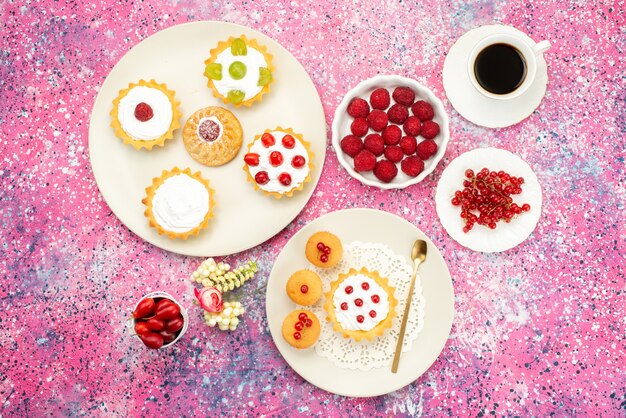 Draufsicht kleine Kuchen mit cremefarbenen frischen Früchten und zusammen mit einer Tasse Kaffee in der weißen Platte auf dem hellen Schreibtischtee