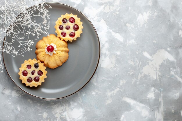 Draufsicht kleine Kuchen mit Früchten innerhalb der grauen Platte auf der hellen Hintergrundkuchenkeks-süßen Zuckerfarbe