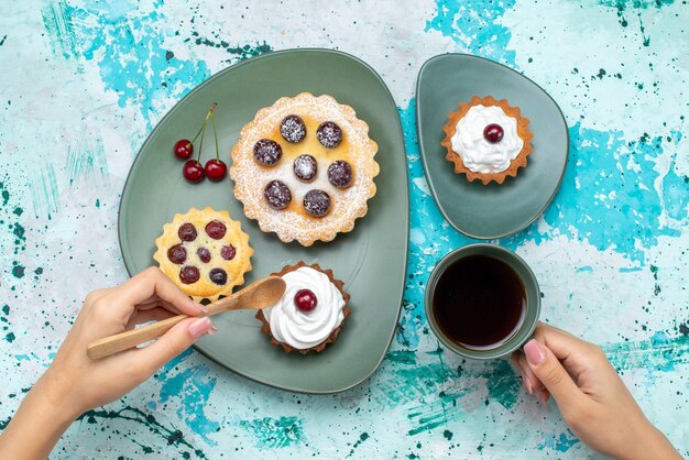 Draufsicht kleine Kuchen mit Zuckerpulverfruchtcreme innerhalbplatte mit Tee auf blauem Schreibtischkuchencremefrucht süßer Tee