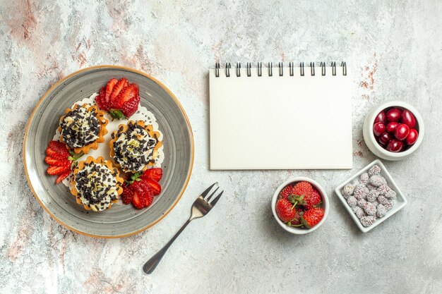 Draufsicht kleine leckere Kuchen mit Erdbeeren auf weißer Oberfläche Geburtstagsfeier süßer Kekskuchen