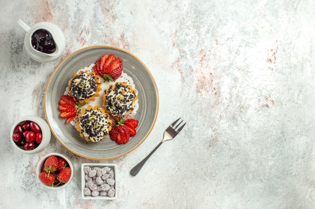 Draufsicht kleine leckere Kuchen mit Sahne und Erdbeeren auf der weißen Oberfläche Geburtstagsfeier süßer Kekskuchen