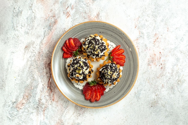 Kostenloses Foto draufsicht kleine leckere kuchen mit sahne und erdbeeren auf weißer oberfläche geburtstagsfeier kuchen süßer keks